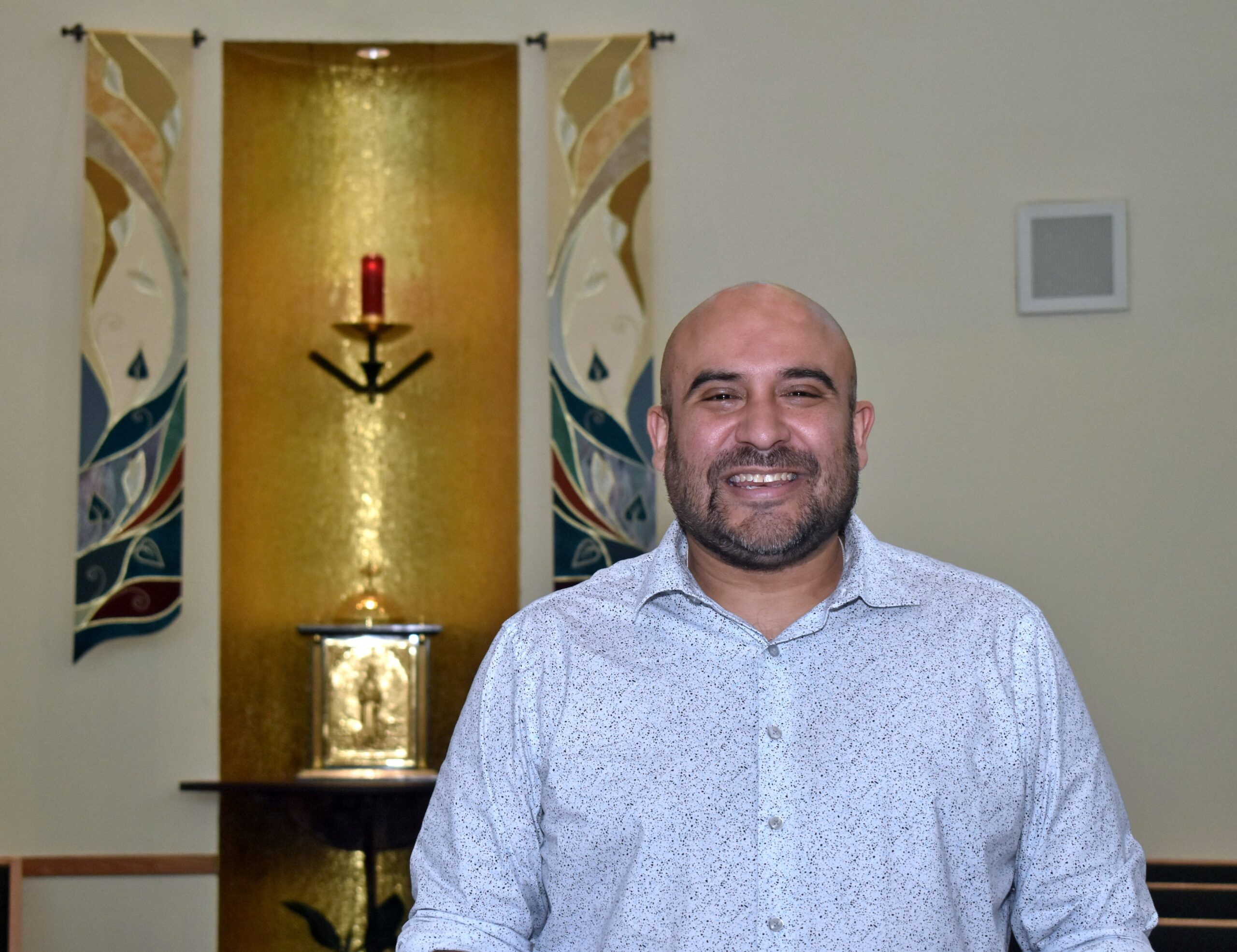 Richard Carrillo poses Aug. 9, 2023, in front of the altar in the chapel of St. John Neumann Church, Miami, where he directs the choir. He's organizing a Mass that blends Aztec and European heritages, "Mass of the Americas," by Los Angeles composer Frank La Rocca, and it will have its Miami premiere the evening of Oct. 3 at Epiphany Church, also in Miami. (OSV News photo/Jim Davis, Florida Catholic)