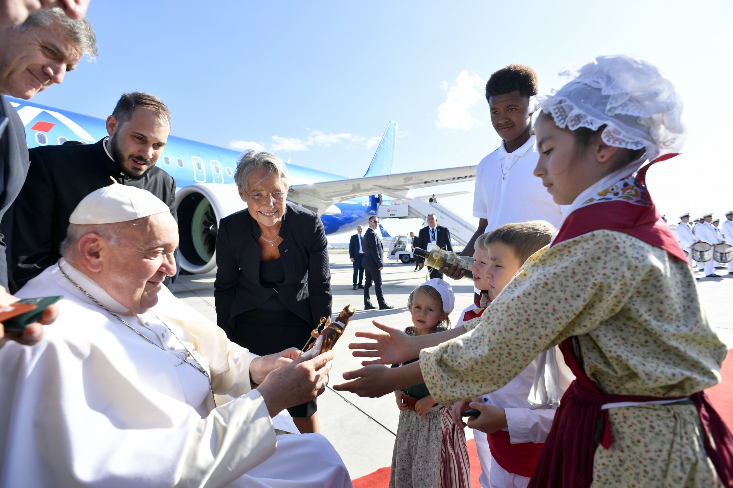 weekly showcase photo: Four children and a young man give Pope Francis gifts while French Prime Minister Élisabeth Borne looks on during a brief welcoming ceremony at Marseille International Airport in Marseille, France, Sept. 22, 2023. (CNS photo/Vatican Media)