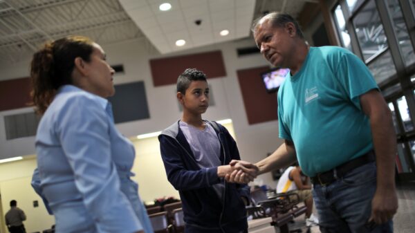 A Catholic Charities worker is pictured in a file photo shaking hands with a young migrant alongside his mother as they prepare to take a bus to Atlanta after being released from a detention center in McAllen, Texas. Among its seven themes, Catholic social teaching emphasizes respect for "the life and dignity of the human person." (OSV News photo/Carlos Barria, Reuters)