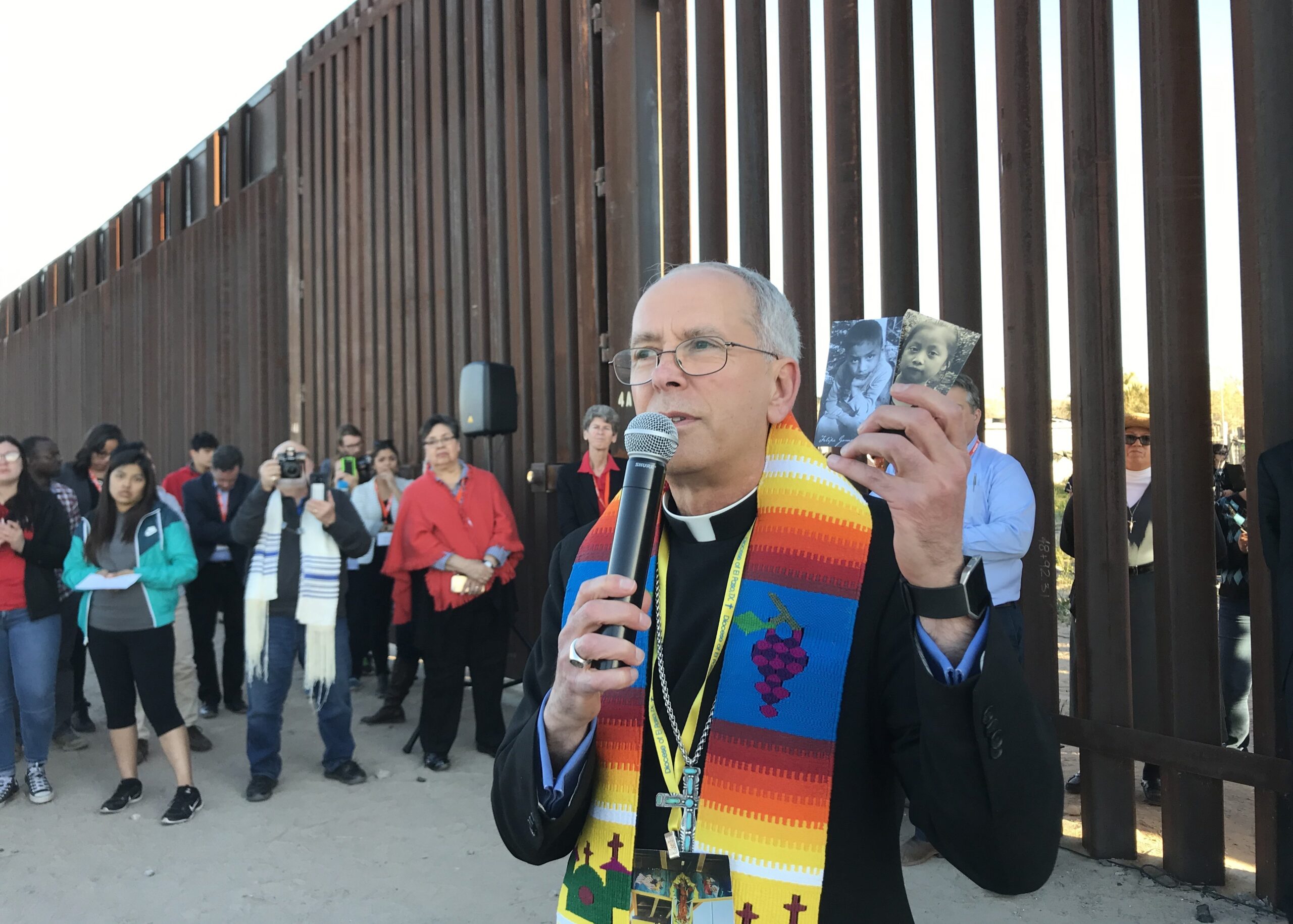 El obispo Mark J. Seitz de El Paso, Texas, es visto el 26 de febrero de 2019, en el muro fronterizo entre Estados Unidos y México sosteniendo fotos de dos niños migrantes que murieron bajo custodia estadounidense. (Foto CNS/David Agren)