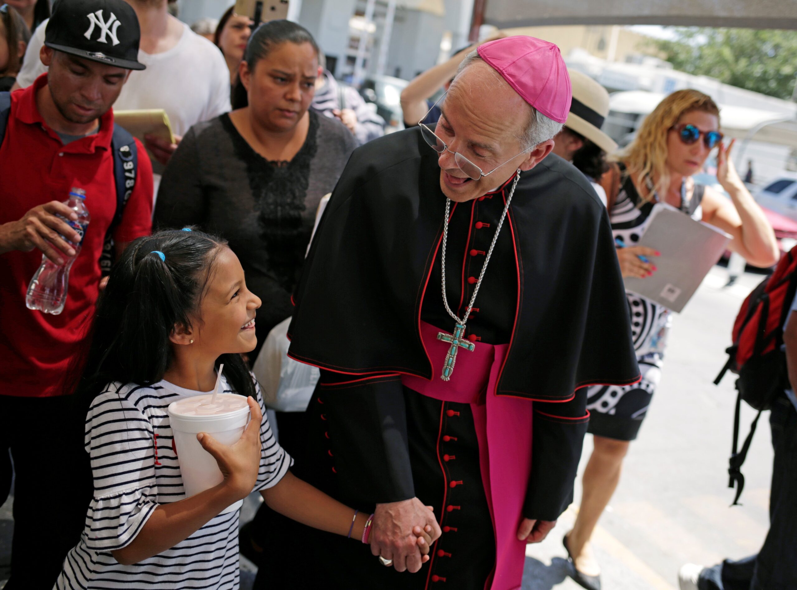 Bishop Mark J. Seitz of El Paso, Texas, shares a smile with a Honduran girl named Cesia as he walks and prays with a group of migrants at the Lerdo International Bridge in El Paso June 27, 2019. (OSV News photo/Jose Luis Gonzalez, Reuters)