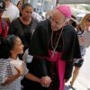 El obispo Mark J. Seitz de El Paso, Texas, comparte una sonrisa con una niña hondureña llamada Cesia mientras camina y reza con un grupo de migrantes en el Puente Internacional Lerdo en El Paso 27 de junio de 2019. (Foto OSV News/Jose Luis González, Reuters)