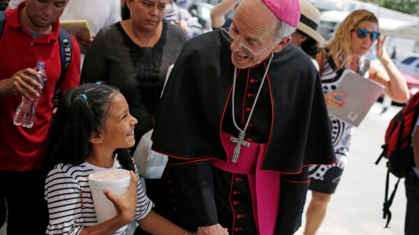 El obispo Mark J. Seitz de El Paso, Texas, comparte una sonrisa con una niña hondureña llamada Cesia mientras camina y reza con un grupo de migrantes en el Puente Internacional Lerdo en El Paso 27 de junio de 2019. (Foto OSV News/Jose Luis González, Reuters)