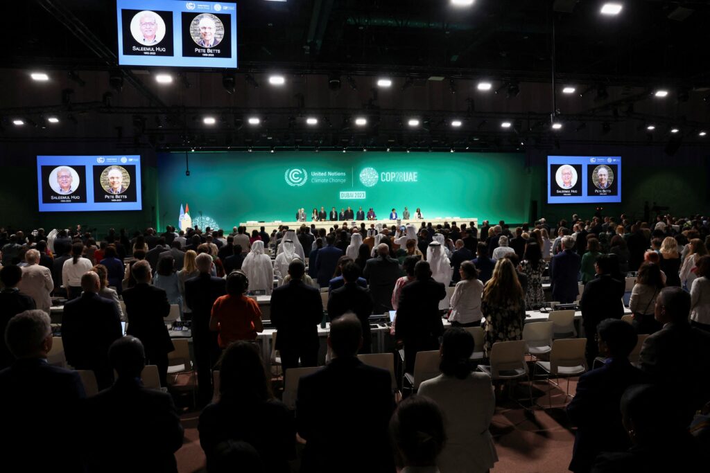 People stand for a moment of silence for victims in Gaza Nov. 30, 2023, during the opening day of the United Nations Climate Change Conference, known as COP28, in Dubai, United Arab Emirates. Efforts to meet climate goals must heed both the 