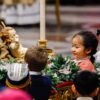 Children place flowers around a figurine of the baby Jesus in front of the main altar of St. Peter’s Basilica during Christmas Mass with Pope Francis at the Vatican Dec. 24, 2023. (CNS photo/Lola Gomez)