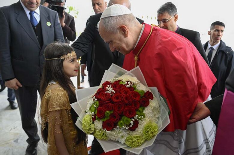 Pope Leo XIV is greeted by an Algerian girl with flowers upon arrival at Houari Boumediene International Airport in Dar El Beida district in Algiers, Algeria, April 13, 2026, to begin his apostolic journey to Algeria, Angola, Cameroon and Equatorial Guinea. (OSV News photo/Simone Risoluti, Vatican Media)