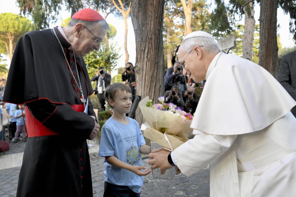 Pope Leo XIV accepts flowers from a child as he is joined by hundreds of children in praying the rosary for peace in the Lourdes Grotto in the Vatican Gardens on the evening of Oct. 1, 2026, the month dedicated to the prayer of the rosary. At left is Cardinal Kurt Koch, prefect of the Dicastery for Promoting Christian Unity. (OSV News photo/Simone Risoluti, Vatican Media)