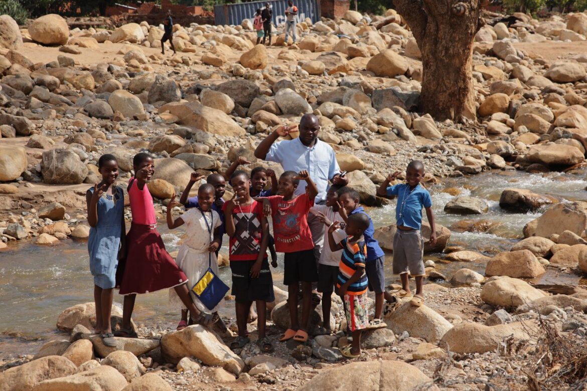 Father Peter Madeya of the Pontifical Mission Societies in Malawi stands with children from the Phalombe district in the remains of a washed-out roadway on the outskirts of the Archdiocese of Blantyre in southern Malawi Dec. 8, 2023. Catholics around the world will mark World Mission Sunday Oct. 18, 2026. (OSV News photo/Margaret Murray)